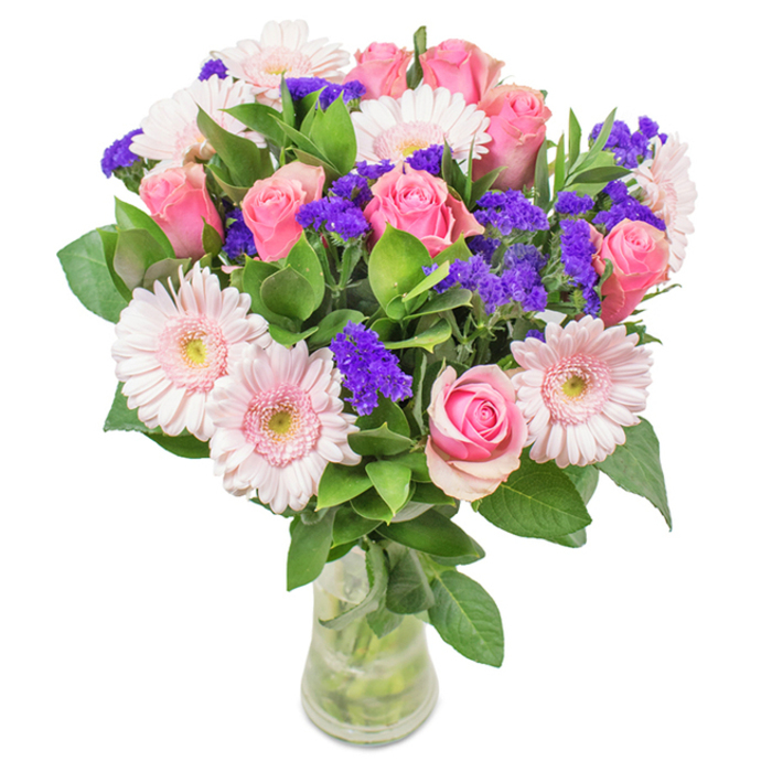 An elegantly arranged bouquet, crafted by a Somers Town florist and presented in a transparent glass vase upon a pristine white surface, captures a luminous harmony of colour and form. The arrangement features seven to nine roses in delicate and medium pink tones-some still tightly furled, others gently opening into their classic spirals-each symbolizing enduring affection or moments of quiet celebration unique to Somers Town. Intertwined with these are five to seven pale pink gerbera daisies, easily identified by their generous round faces and radiating petals tipped with creamy centers. Between each focal bloom, clusters of vivid purple statice or limonium rise, offering both texture and a dynamic pop of deeper colour that feels reminiscent of the colourful stalls at Somers Town Market. Lush, dark green foliage encircles the arrangement, imparting a sense of contemporary abundance and echoing the greenery in Oakshott Court or Granary Square. The clear vase showcases freshly cut stems and pure water, accentuating the authenticity and freshness of each flower-a signature of local Somers Town delivery. Perfect for personal celebrations, from birthdays in the heart of the neighbourhood to office gestures along Eversholt Street, this bouquet radiates joy, grace, and the rich affection of community ties.